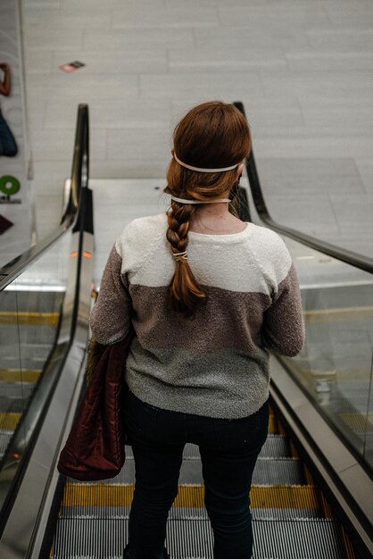 Vista trasera de una mujer de pie en una escalera mecánica