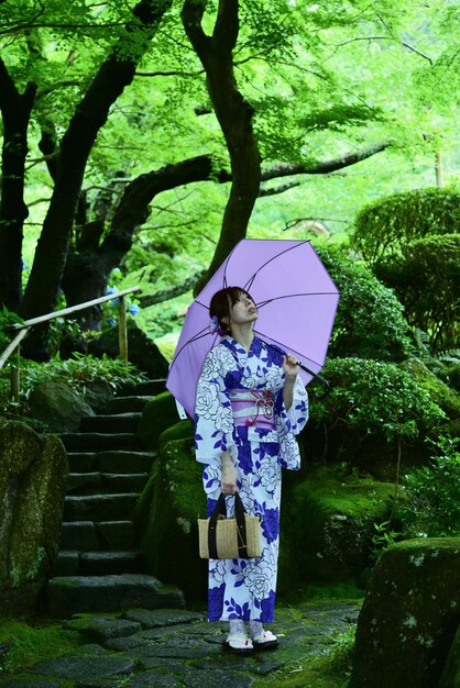 Foto vista trasera de una mujer de pie junto a un árbol sosteniendo un paraguas durante la lluvia
