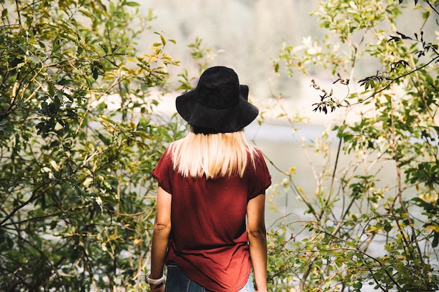 Vista trasera de una mujer de pie junto a las plantas y el lago