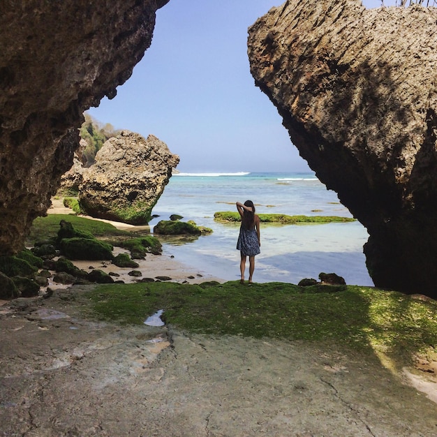 Foto vista trasera de una mujer de pie en medio de formaciones rocosas frente al mar