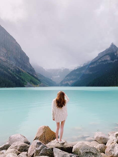 Foto vista trasera de una mujer de pie en la orilla del lago contra las montañas