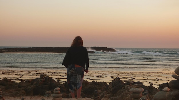 Vista trasera de una mujer de pie en la playa contra un cielo despejado