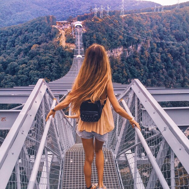 Foto vista trasera de una mujer de pie en un puente de metal.