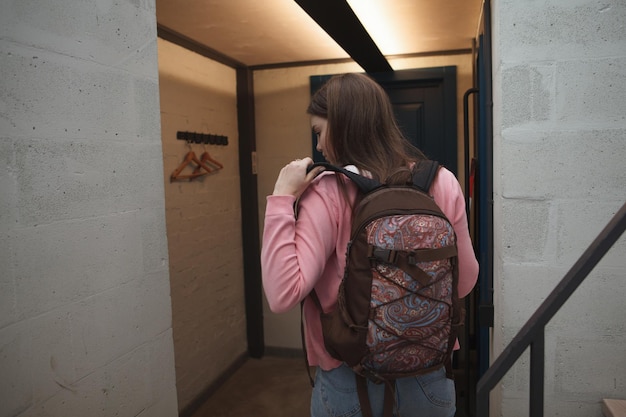 Vista trasera de una mujer poniéndose la mochila antes de salir de la habitación del hotel