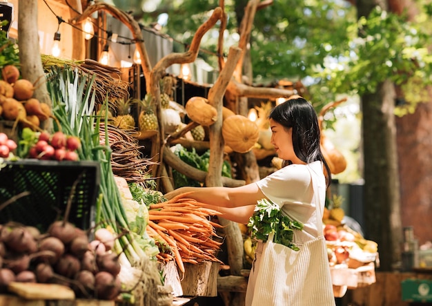 Vista trasera de una mujer recogiendo verduras para la venta en el mercado