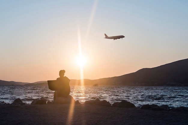 Vista trasera de una mujer relajándose en la orilla al atardecer