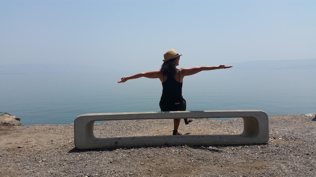 Foto vista trasera de una mujer sentada en un asiento de hormigón por la orilla del lago contra el cielo