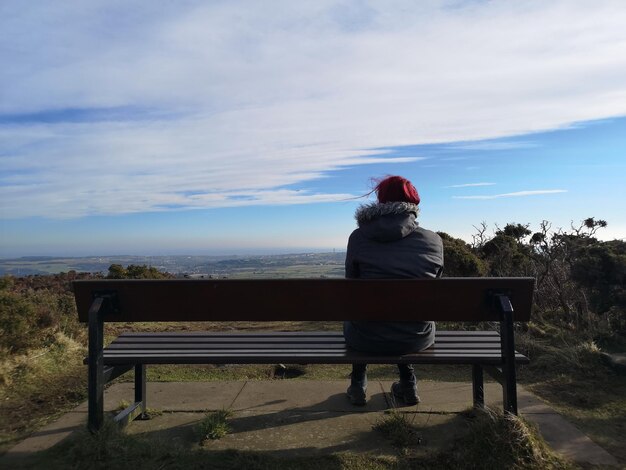 Foto vista trasera de una mujer sentada en un banco contra el cielo