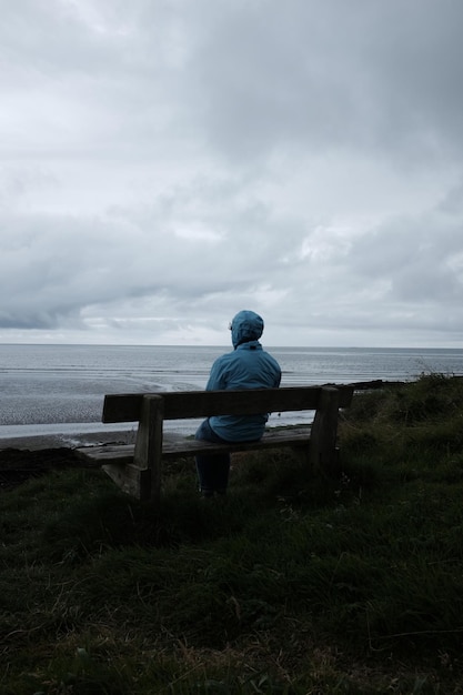 Vista trasera de una mujer sentada en un banco junto al mar contra el cielo