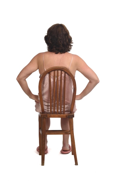 Vista trasera de una mujer sentada con camisón sobre fondo blanco,
