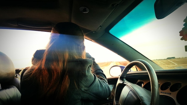 Vista trasera de una mujer sentada en un coche contra el cielo