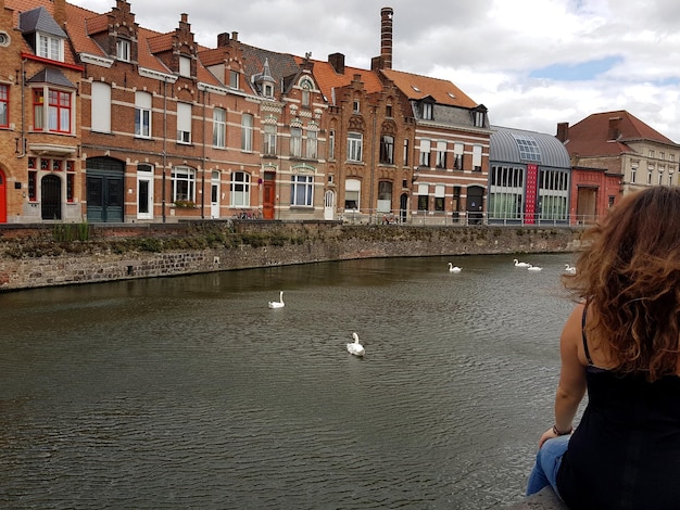 Foto vista trasera de una mujer sentada contra un canal en la ciudad