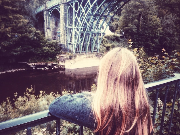 Foto vista trasera de una mujer sentada contra un puente