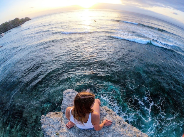 Foto vista trasera de una mujer sentada en una formación rocosa junto al mar