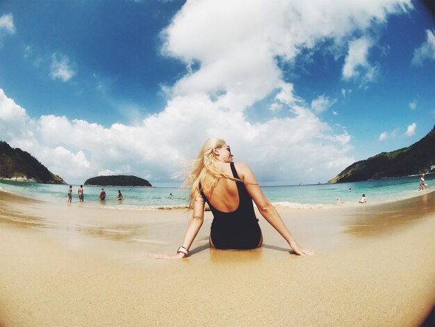 Foto vista trasera de una mujer sentada en la playa contra un cielo nublado