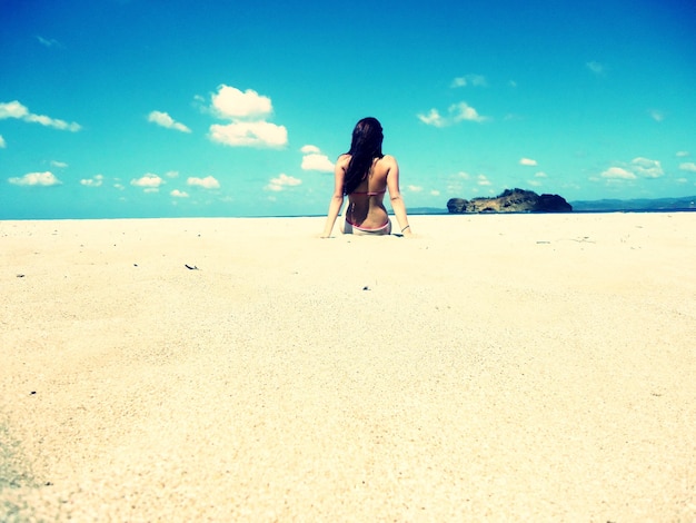 Foto vista trasera de una mujer sentada en la playa