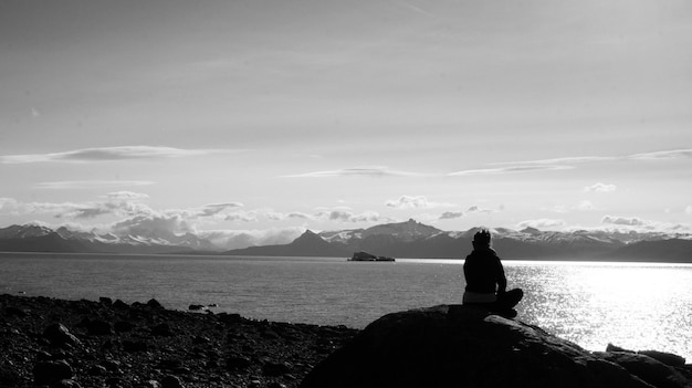 Foto vista trasera de una mujer sentada en una roca contra el mar