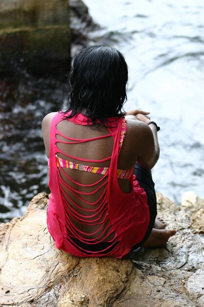 Vista trasera de una mujer sentada en una roca junto al lago