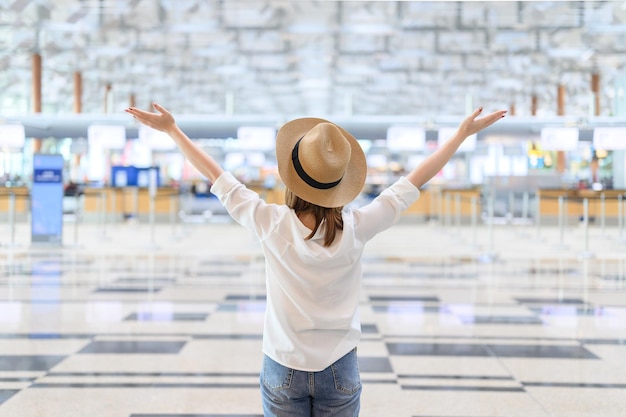 Foto vista trasera de una mujer con sombrero y brazos levantados de pie en el aeropuerto