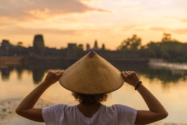 Foto vista trasera de una mujer con sombrero contra el lago durante la puesta de sol