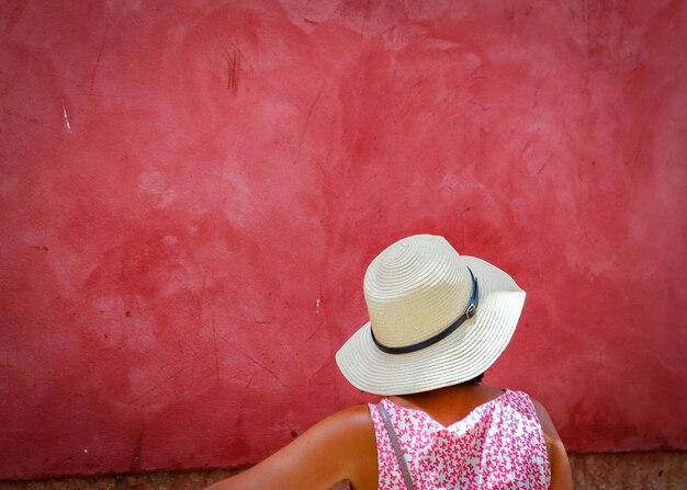 Vista trasera de una mujer con sombrero contra una pared roja