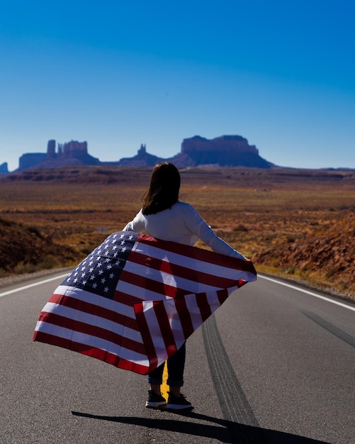 Foto vista trasera de una mujer sosteniendo una bandera mientras está de pie en la carretera