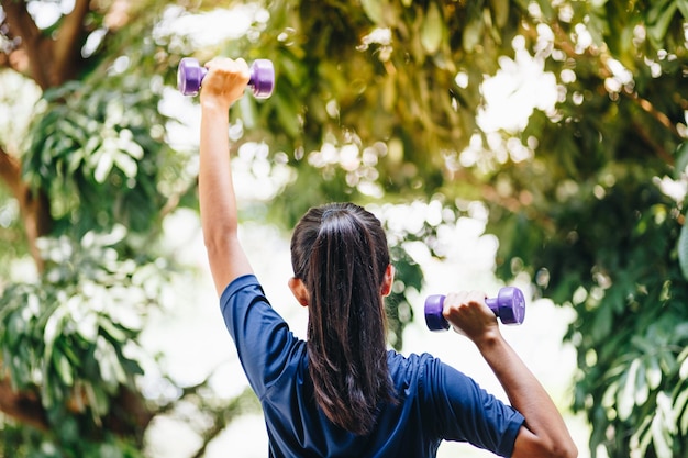 Foto vista trasera de una mujer sosteniendo pesas mientras hace ejercicio al aire libre