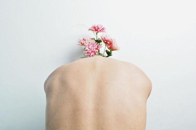 Vista trasera de una mujer en topless con flores contra la pared