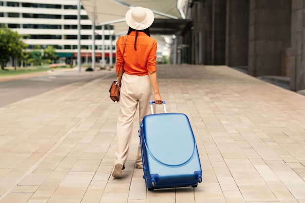 Vista trasera de una mujer turista caminando con una maleta cerca del aeropuerto