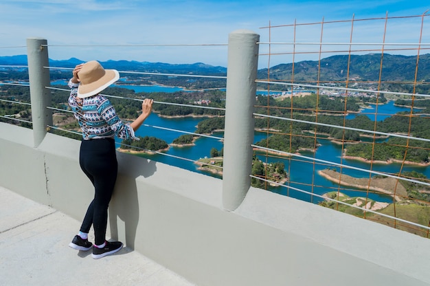 Vista trasera de la mujer turista con sombrero contemplando la naturaleza en Guatape Colombia desde Penol Stone