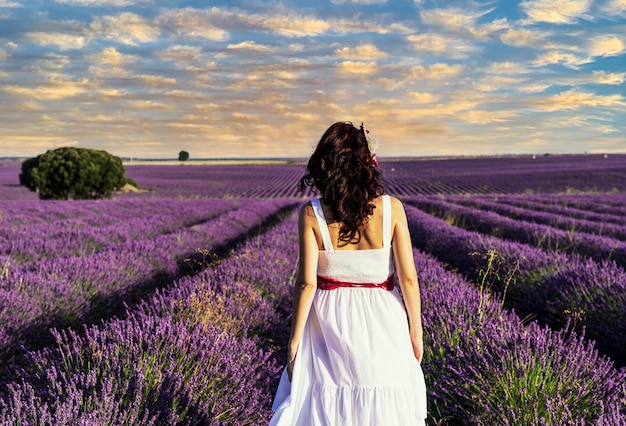 Vista trasera de una mujer con un vestido caminando en un campo de flores de lavanda