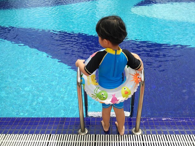 Foto vista trasera de una niña en un anillo inflable de pie a la orilla de la piscina