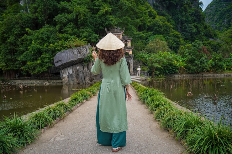 Foto vista trasera de una niña con ao dai frente a un paisaje de parque al aire libre con lago y puente de piedra entrada al antiguo complejo de la pagoda bich dong destino de viaje de ninh binh vietnam