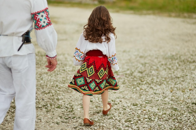 Vista trasera de una niña caminando con su padre afuera usando ropa tradicional eslava