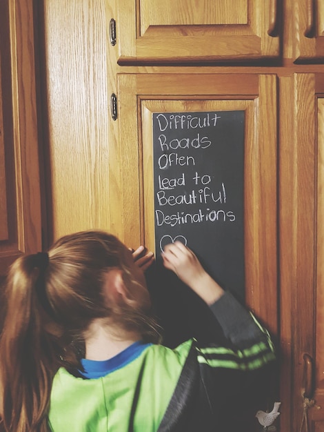 Foto vista trasera de una niña escribiendo con tiza en la puerta