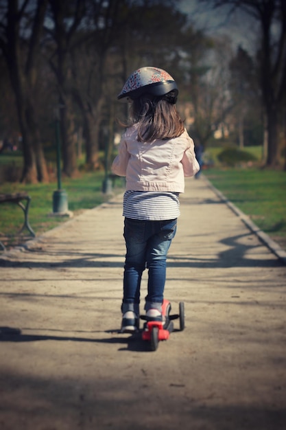 Vista trasera de una niña montando un scooter de empuje en un sendero en el parque