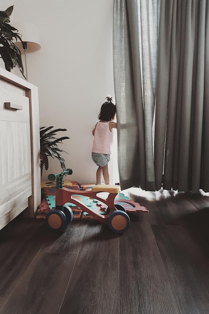 Vista trasera de una niña de pie junto a la cortina en casa