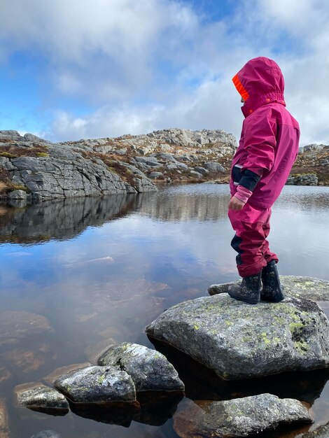 Foto vista trasera de una niña de pie en una roca contra el cielo