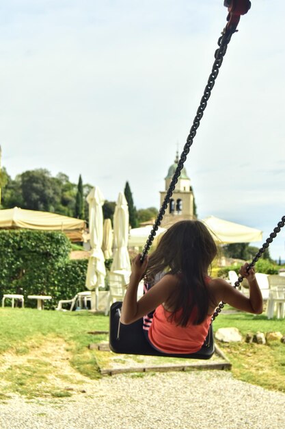 Vista trasera de una niña sentada en un columpio en el patio de recreo