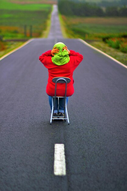 Vista trasera de una niña sentada en una silla sobre la carretera