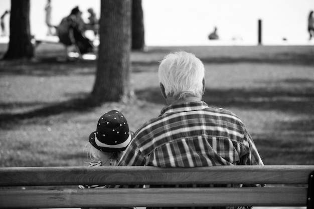 Vista trasera de una niña con su abuelo sentado en un banco en el parque