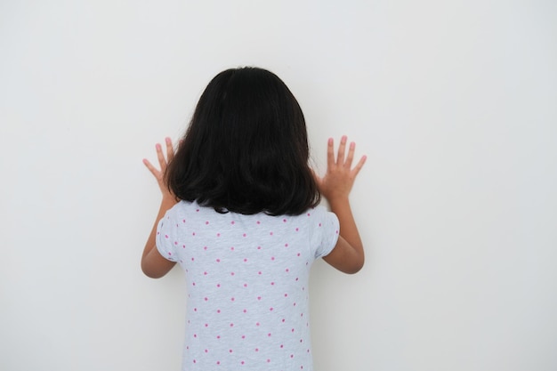 Foto vista trasera del niño asiático frente a la pared que muestra una emoción triste