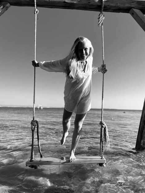 Vista trasera de un niño balanceándose en la playa contra el cielo