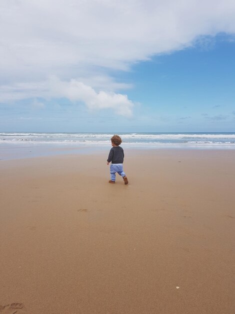 Foto vista trasera de un niño caminando por la playa contra el cielo