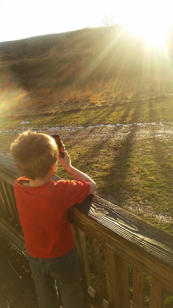 Foto vista trasera de un niño fotografiando el campo en un día soleado