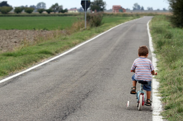 Foto vista trasera de un niño montando una bicicleta en la carretera