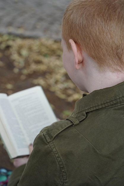 Vista trasera de un niño pelirrojo leyendo un libro