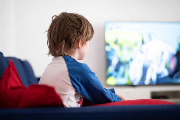 Vista trasera de un niño pequeño sentado en un sofá viendo la televisión