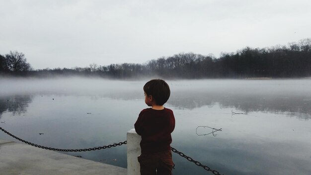 Foto vista trasera de un niño de pie en el muelle sobre el lago contra el cielo