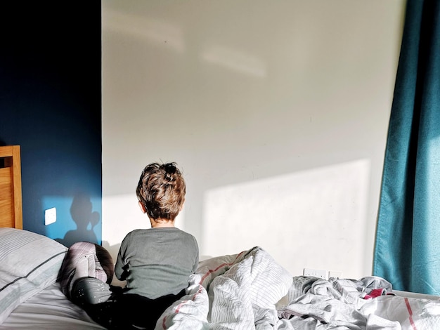 Vista trasera de un niño sentado en la cama en casa